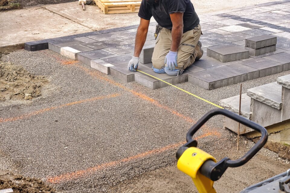 Landscaping contractor worker using tape measure ruler measuring and laying interlock stones on a construction site.